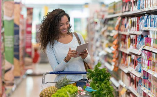 African american woman shopping at the supermarket and looking at the shopping list on a digital tablet looking very happy and smiling